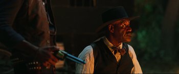 Movie still from “The Harder They Fall” (2021), directed by Jeymes Samuel – A man in a hat and vest holding a gun; Close Up shot, Over the shoulder angle