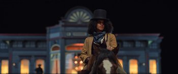 Movie still from “The Harder They Fall” (2021), directed by Jeymes Samuel – A woman riding on the back of a brown horse; Medium shot, Low angle
