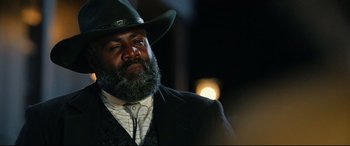 Movie still from “The Harder They Fall” (2021), directed by Jeymes Samuel – A man with a beard wearing a cowboy hat; Close Up shot, Low angle