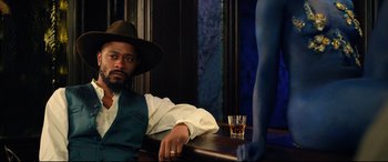 Movie still from “The Harder They Fall” (2021), directed by Jeymes Samuel – A man sitting at a table in front of a glass of whiskey; Medium shot, Over the shoulder angle