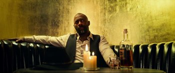 Movie still from “The Harder They Fall” (2021), directed by Jeymes Samuel – A man sitting in front of a lit candle; Medium shot, Low angle
