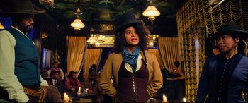 Movie still from “The Harder They Fall” (2021), directed by Jeymes Samuel – A woman wearing a black hat and a brown jacket; Medium shot, Low angle