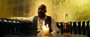 Movie still from “The Harder They Fall” (2021), directed by Jeymes Samuel – A man sitting in front of a candle on a table; Medium shot, Low angle