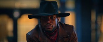 Movie still from “The Harder They Fall” (2021), directed by Jeymes Samuel – A man wearing a black hat and a brown jacket; Close Up shot, Low angle
