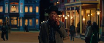 Movie still from “The Harder They Fall” (2021), directed by Jeymes Samuel – A man wearing a cowboy hat while talking on a cell phone; Medium shot, Over the shoulder angle
