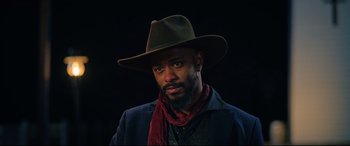 Movie still from “The Harder They Fall” (2021), directed by Jeymes Samuel – A man wearing a hat and a scarf; Close Up shot, Low angle