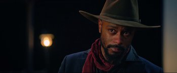 Movie still from “The Harder They Fall” (2021), directed by Jeymes Samuel – A person wearing a hat and a scarf; Close Up shot, Over the shoulder angle