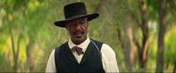Movie still from “The Harder They Fall” (2021), directed by Jeymes Samuel – A man wearing a black hat and a white shirt; Close Up shot, Low angle