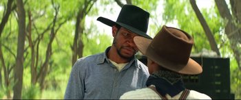 Movie still from “The Harder They Fall” (2021), directed by Jeymes Samuel – A man wearing a cowboy hat talking to another man; Close Up shot, Over the shoulder angle