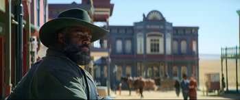 Movie still from “The Harder They Fall” (2021), directed by Jeymes Samuel – A man with a beard wearing a green hat; Medium shot, Low angle