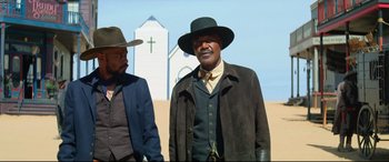 Movie still from “The Harder They Fall” (2021), directed by Jeymes Samuel – A man in a hat standing next to another man in a suit; Medium shot, Low angle