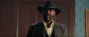 Movie still from “The Harder They Fall” (2021), directed by Jeymes Samuel – A man wearing a suit and a black hat; Medium shot, Low angle