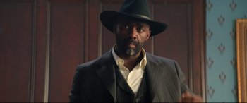 Movie still from “The Harder They Fall” (2021), directed by Jeymes Samuel – A man wearing a suit and a black hat; Close Up shot, Low angle