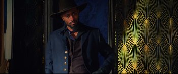 Movie still from “The Harder They Fall” (2021), directed by Jeymes Samuel – A man wearing a black hat and a blue jacket; Medium shot, Low angle