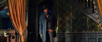 Movie still from “The Harder They Fall” (2021), directed by Jeymes Samuel – A man standing in front of a door wearing a hat; Medium shot, Low angle