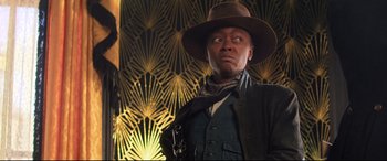 Movie still from “The Harder They Fall” (2021), directed by Jeymes Samuel – A man in a hat and a jacket holding a gun; Medium shot, Low angle