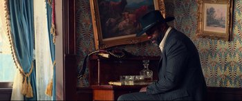 Movie still from “The Harder They Fall” (2021), directed by Jeymes Samuel – A man sitting in front of a painting; Medium shot, Low angle