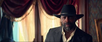 Movie still from “The Harder They Fall” (2021), directed by Jeymes Samuel – A man wearing a suit and a black hat; Close Up shot, Low angle