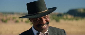 Movie still from “The Harder They Fall” (2021), directed by Jeymes Samuel – An older man wearing a hat and a bow tie; Close Up shot, Low angle