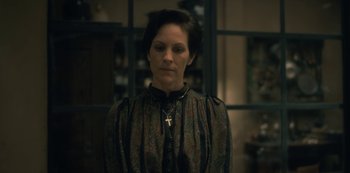 Movie still from “The Haunting of Hill House” (2018), directed by Mike Flanagan – A woman wearing a black and green dress with a cross on it; Medium shot, High angle