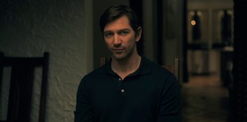 Movie still from “The Haunting of Hill House” (2018), directed by Mike Flanagan – A person sitting in a chair wearing a polo shirt; Medium shot, Over the shoulder angle