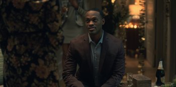 Movie still from “The Haunting of Hill House” (2018), directed by Mike Flanagan – A man in a brown suit sitting in front of a table; Medium shot, Over the shoulder angle