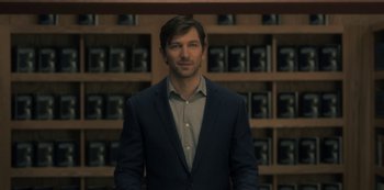 Movie still from “The Haunting of Hill House” (2018), directed by Mike Flanagan – A man standing in front of a shelf of tea bags; Medium shot, Over the shoulder angle