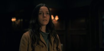 Movie still from “The Haunting of Hill House” (2018), directed by Mike Flanagan – A woman in a brown coat standing in a dark room; Close Up shot, Low angle