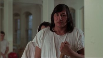 Movie still from “One Flew Over the Cuckoo's Nest” (1975), directed by Milos Forman – A man with long black hair holding a wooden stick; Medium shot, Low angle