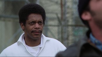 Movie still from “One Flew Over the Cuckoo's Nest” (1975), directed by Milos Forman – A man in a white shirt is standing in front of a chain link fence; Close Up shot, Low angle