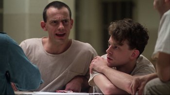 Movie still from “One Flew Over the Cuckoo's Nest” (1975), directed by Milos Forman – Two men are sitting at a table and one of the men has his hands on his chest; Close Up shot, Low angle