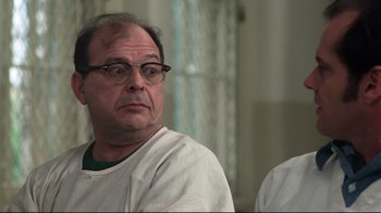 Movie still from “One Flew Over the Cuckoo's Nest” (1975), directed by Milos Forman – An older man wearing glasses sitting in front of a window; Close Up shot, Over the shoulder angle