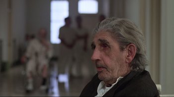 Movie still from “One Flew Over the Cuckoo's Nest” (1975), directed by Milos Forman – An older man sitting in front of a group of people; Close Up shot, Over the shoulder angle