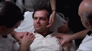 Movie still from “One Flew Over the Cuckoo's Nest” (1975), directed by Milos Forman – A man in a hospital bed being examined by two doctors; Medium shot, Over the shoulder angle