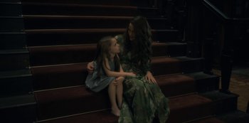 Movie still from “The Haunting of Hill House” (2018), directed by Mike Flanagan – A woman sitting on the stairs with a little girl; Medium shot, High angle
