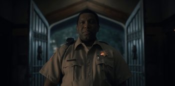 Movie still from “The Haunting of Hill House” (2018), directed by Mike Flanagan – A man in a brown uniform standing next to a building; Close Up shot, Low angle