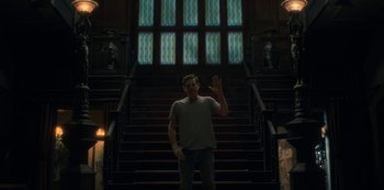 Movie still from “The Haunting of Hill House” (2018), directed by Mike Flanagan – A man standing in front of a set of stairs; Wide shot, Low angle