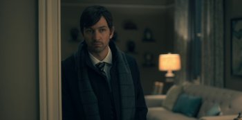 Movie still from “The Haunting of Hill House” (2018), directed by Mike Flanagan – A man wearing a jacket and tie in a living room; Medium shot, Over the shoulder angle