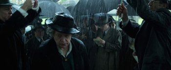 Movie still from “The Highwaymen” (2019), directed by John Lee Hancock – A group of people standing in the rain under umbrellas; Medium shot, Over the shoulder angle