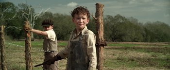 Movie still from “The Highwaymen” (2019), directed by John Lee Hancock – A young boy standing next to a wooden pole; Medium shot, Low angle