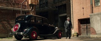Movie still from “The Highwaymen” (2019), directed by John Lee Hancock – A man standing next to an antique car; Wide shot, Low angle