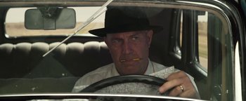 Movie still from “The Highwaymen” (2019), directed by John Lee Hancock – A man in a hat is sitting in the drivers seat of a car; Close Up shot, Low angle