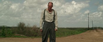 Movie still from “The Highwaymen” (2019), directed by John Lee Hancock – An old man standing on a dirt road in the middle of a field; Medium shot, Low angle