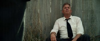 Movie still from “The Highwaymen” (2019), directed by John Lee Hancock – A man in a white shirt and black tie sitting in front of a wooden fence; Medium shot, Low angle