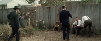 Movie still from “The Highwaymen” (2019), directed by John Lee Hancock – A man in a suit and hat walking in a yard; Wide shot, High angle