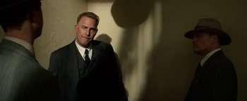 Movie still from “The Highwaymen” (2019), directed by John Lee Hancock – A man wearing a suit and tie standing in front of a wall; Medium shot, Low angle