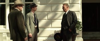 Movie still from “The Highwaymen” (2019), directed by John Lee Hancock – A man in a suit and a man in a hat talking to each other; Medium shot, Low angle