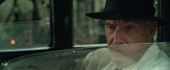 Movie still from “The Highwaymen” (2019), directed by John Lee Hancock – A man wearing a hat sitting in the back seat of a car; Close Up shot, Over the shoulder angle