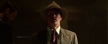 Movie still from “The Highwaymen” (2019), directed by John Lee Hancock – A man wearing a suit and a hat in a dark room; Close Up shot, Low angle