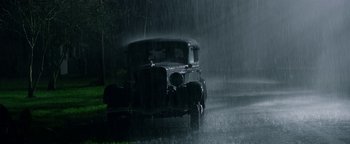 Movie still from “The Highwaymen” (2019), directed by John Lee Hancock – An old car driving down the street in the rain; Wide shot, High angle